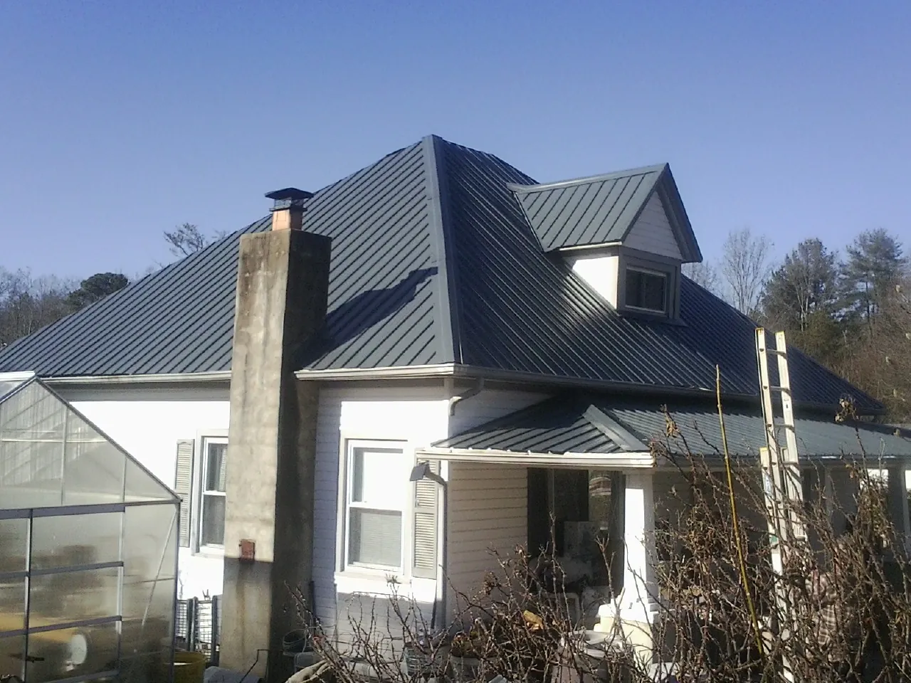 Dark blue standing seam metal roof on a white farmhouse with dormer in Nome
