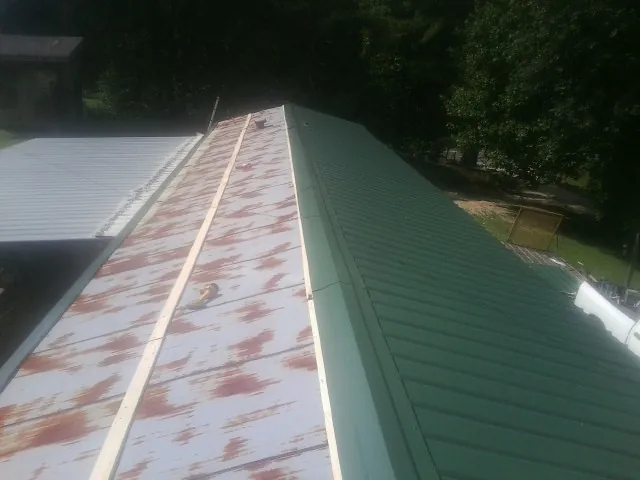 Old rusted panels beside newly installed green metal roofing — Wind Damage Roof Repair by Roofing Brothers in Nome
