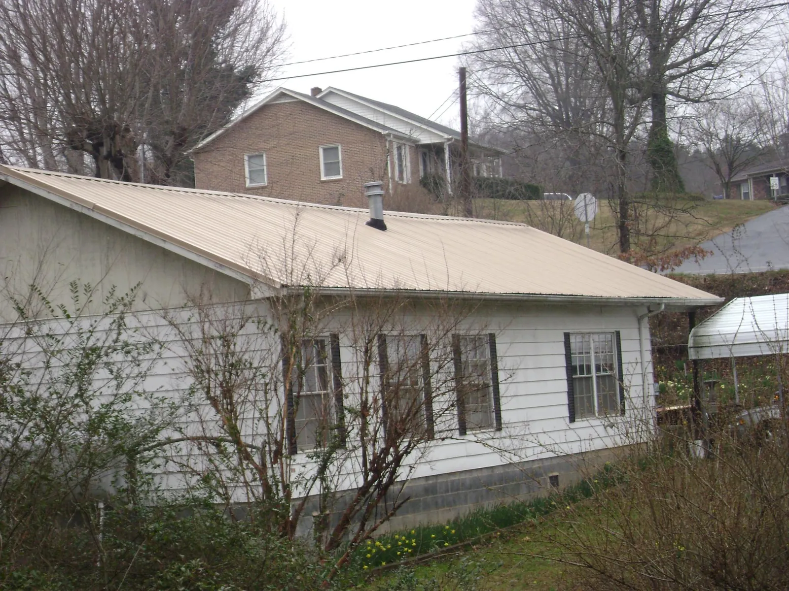 Tan metal roof on a white sided house set into a hillside — Commercial Roofing by Roofing Brothers in Nome