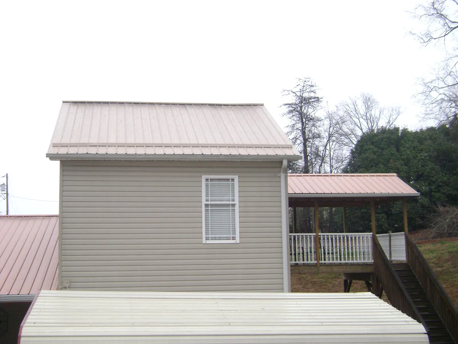 Tan metal roofs on a two story addition and attached porch, from a Roof Replacement job in Nome
